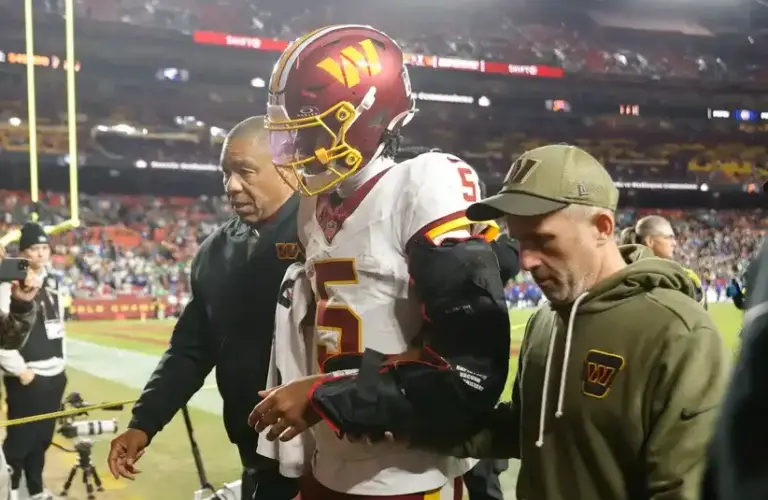 Jayden Daniels is supported by two staff members off the field.