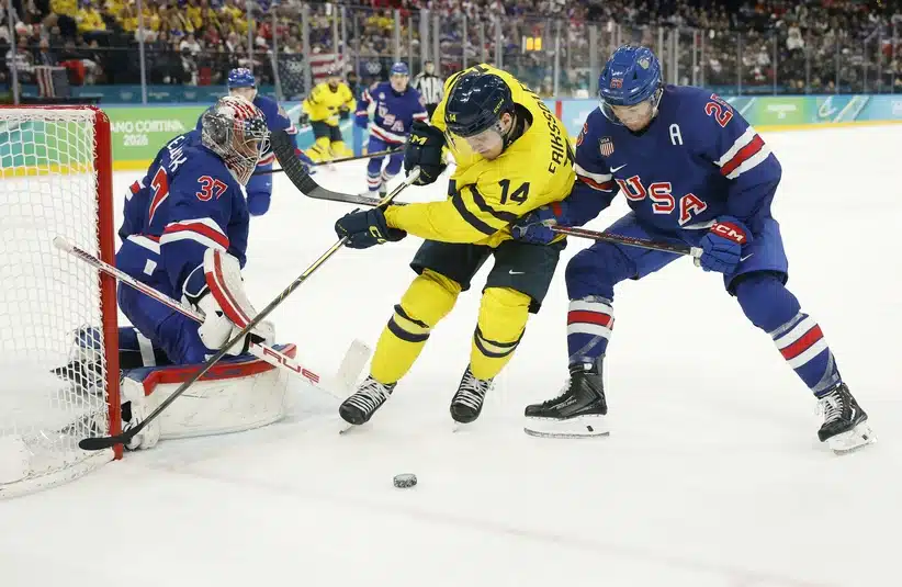 February 18, 2026; Milan, Italy; Joel Eriksson Ek (14) of Sweden battles for the puck between Connor Hellebuyck (37) of the United States and Charlie McAvoy (25) of the United States in a men's ice hockey quarterfinal during the Milano Cortina 2026 Olympic Winter Games at Milano Santa Giulia Ice Hockey Arena.