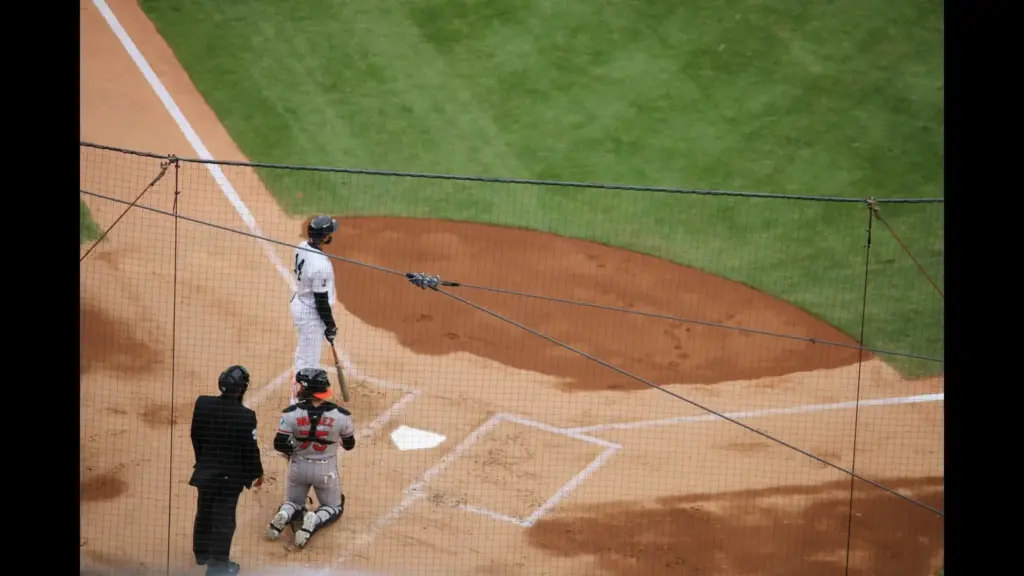 A baseball player stands at home plate in a baseball stadium, with a catcher in gear squatting behind him and an umpire in the foreground. Yankees, Orioles, Doubleheader, MLB